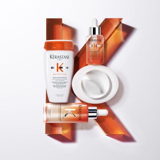 Three Kérastase hair care products displayed on a white surface, featuring a shampoo, oil, and mask, with orange accents.